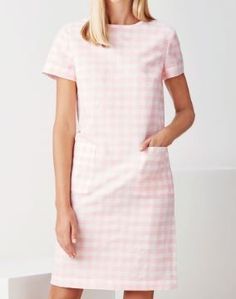 a woman standing in front of a white wall wearing a pink checkered shift dress