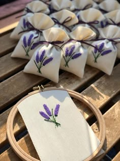 some purple flowers are sitting on a table next to a cross stitch pattern and a wooden hoop