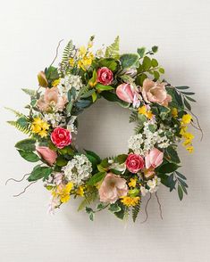 a wreath with flowers and greenery is hanging on the side of a white wall