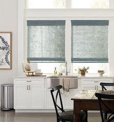 a kitchen with white cabinets and windows covered in roman shades, along with a dining table set for four