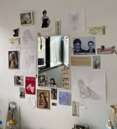 a white wall covered in pictures and drawings on it's side with a mirror