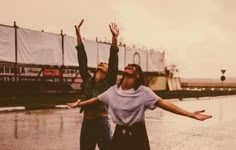 two people standing in the rain with their arms up and one person holding an umbrella