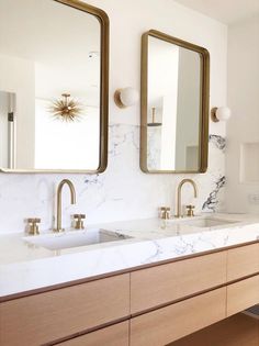 a bathroom with marble counter tops and gold framed mirrors on the wall, along with two sinks