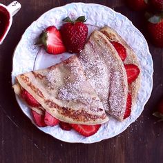 pancakes with powdered sugar and strawberries are on a white plate next to syrup