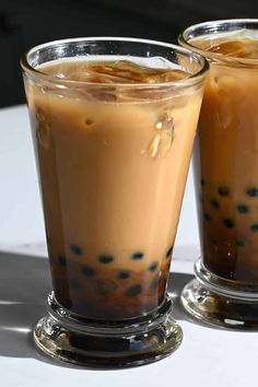 two glasses filled with iced coffee sitting on top of a white table next to each other