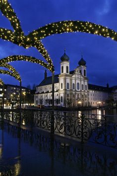 the lights are hanging over the water in front of an ornate building with arches and columns