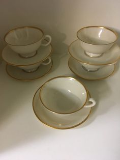 five white and gold china cups and saucers on a counter top, with one empty cup in the middle