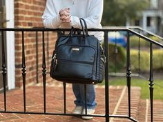 a woman holding onto a black purse on top of a metal hand rail next to a brick building