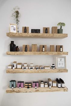 three wooden shelves filled with different types of cosmetics on top of each other in front of a white wall