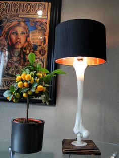 a table with a lamp, potted lemons and a painting on the wall