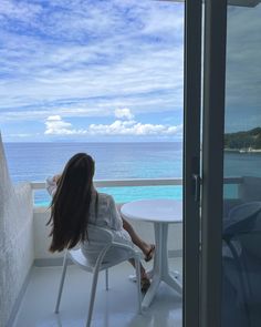 a woman sitting at a table on top of a balcony next to the ocean,