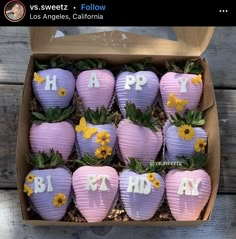 a box filled with lots of purple strawberries covered in frosting and topped with flowers