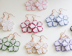 six pairs of flower shaped earrings sitting on top of a white table next to each other