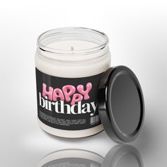 a white candle with a black lid and the words happy birthday in pink on it