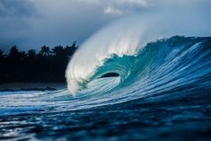 a large wave is breaking in the ocean with blue water and dark clouds above it