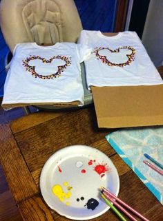 two t - shirts with beaded designs on them are sitting on a table next to paintbrushes