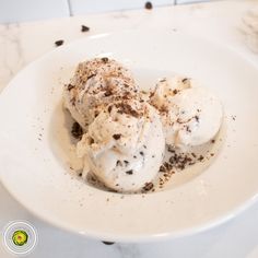 three scoops of ice cream in a white bowl on a marble counter top with chocolate sprinkles