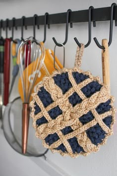 a crocheted pot holder hanging on a wall with kitchen utensils in the background