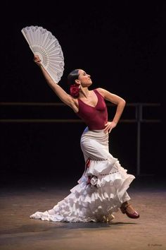 a woman in a red top and white skirt is holding an umbrella while standing on a stage