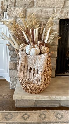 a wicker basket filled with white pumpkins and dry grass in front of a fireplace