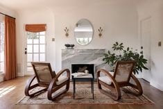 a living room with two chairs and a mirror on the wall next to a fireplace