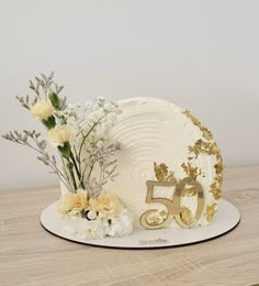 a 50th birthday cake with flowers and gold numbers on it, sitting on a table