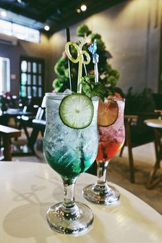 two glasses filled with different colored drinks on top of a table