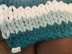 a blue and white crocheted blanket sitting on top of a brown leather couch