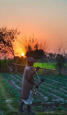 a man standing in the middle of a field holding a stick and wearing a hat