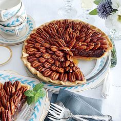 two pies with pecans on top are sitting on plates next to cups and saucers