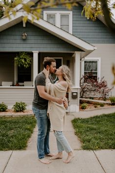 a man and woman standing in front of a house with their arms around each other