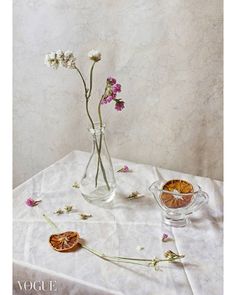 a table topped with a vase filled with flowers next to an empty glass cup and saucer