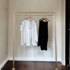 two white shirts hanging on clothes racks in front of a wall and wooden flooring