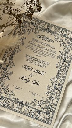 an ornate wedding card on a white satin sheet with dried flowers in the foreground