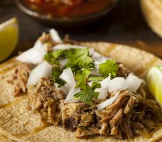 a tortilla topped with shredded meat, cilantro and lime wedges