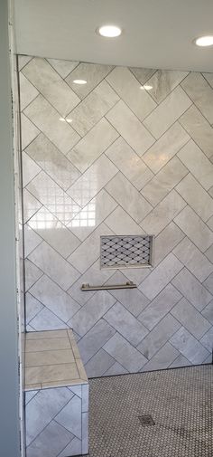 a walk in shower sitting next to a white tiled wall with a metal grate on the side