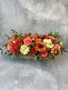 an arrangement of flowers in a vase on a gray surface with leaves and branches around it