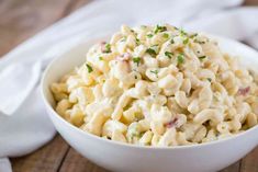 a white bowl filled with macaroni salad on top of a wooden table