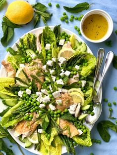 a white plate topped with a salad covered in peas and cucumbers next to lemons