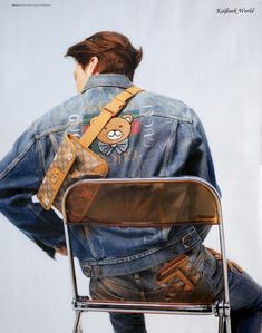 a man sitting on top of a metal chair wearing a jean jacket and carrying a teddy bear bag