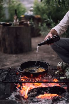 a person pouring water into a skillet over an open fire