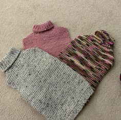 three knitted mittens laying on the floor next to each other, one pink and one gray