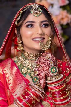 a woman in red and gold bridal outfit with jewelry on her face, smiling at the camera