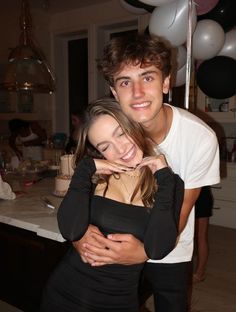 a man and woman hugging each other in the kitchen with balloons all around their necks