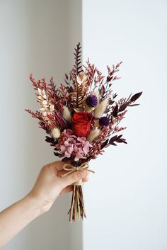 a person holding a bouquet of flowers in their hand with white walls behind them and a wall to the side