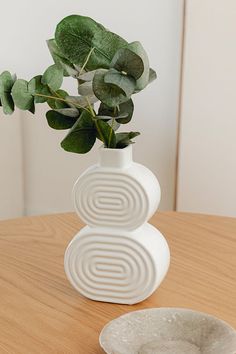 a white vase sitting on top of a wooden table next to a bowl filled with leaves