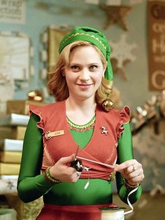 a woman in a green and red outfit is holding a pair of scissors while smiling