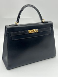 This is the authentic HERMES Box Kelly Sellier 28 in Black.  This handbag is crafted of calfskin leather in black. This bag features a rolled leather top handle and polished gold plated hardware.  The flap opens with a signature Kelly turn lock to a matching black leather interior with zipper and patch pockets. WE ARE NOT AFFILIATED WITH HERMES This item is in C condition (see table below). We do offer local pickup from our shop. For sales made within California, we charge sales tax of 9.25%. Let us know if you have any questions. We would like to make your transactions with us as smooth as possible. Please read the item descriptions carefully and look at all the pictures closely to make sure the item is exactly what you want. If there are any discrepancies or confusion, send us a message Kelly Sellier, Hermes Box, Black Handbag, Sales Tax, Black Handbags, Leather Interior, Leather Top, Patch Pocket, Top Handle