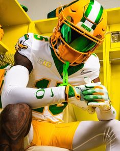 a football player in green and white uniform sitting on a yellow bench with his hands clasped