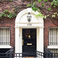 an entrance to a brick building with wrought iron railings and black door, surrounded by greenery